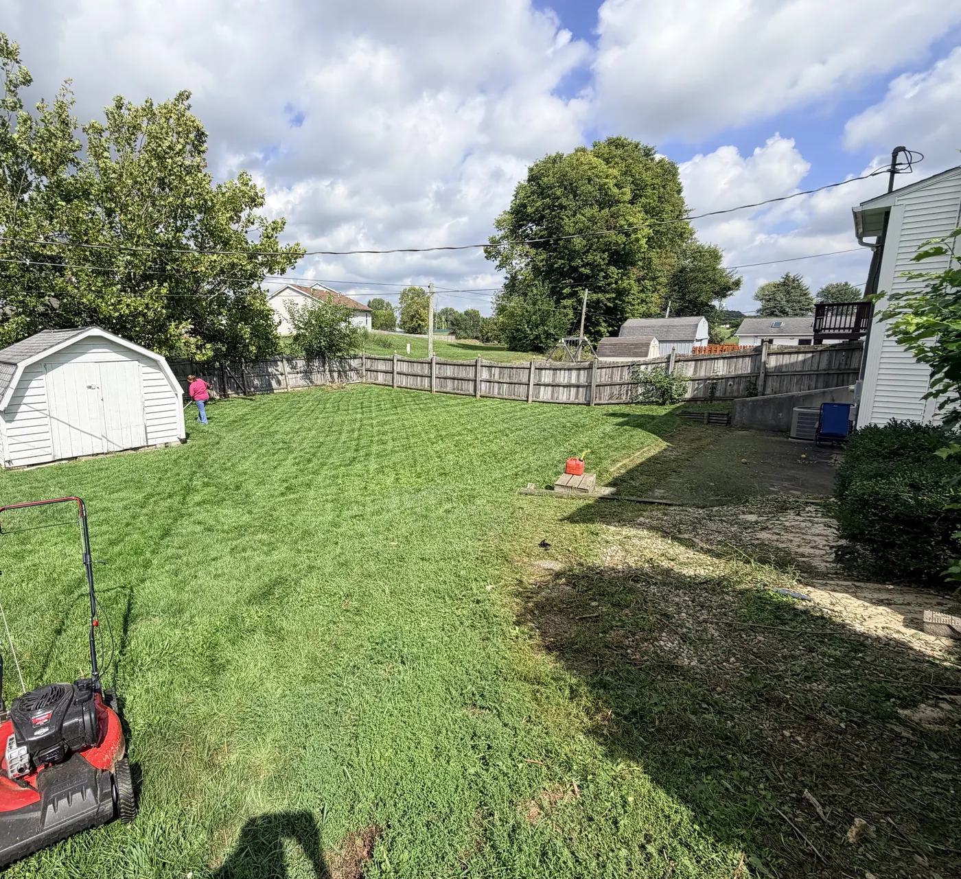 Wide fenced back yard, freshly cut, with a red push mower