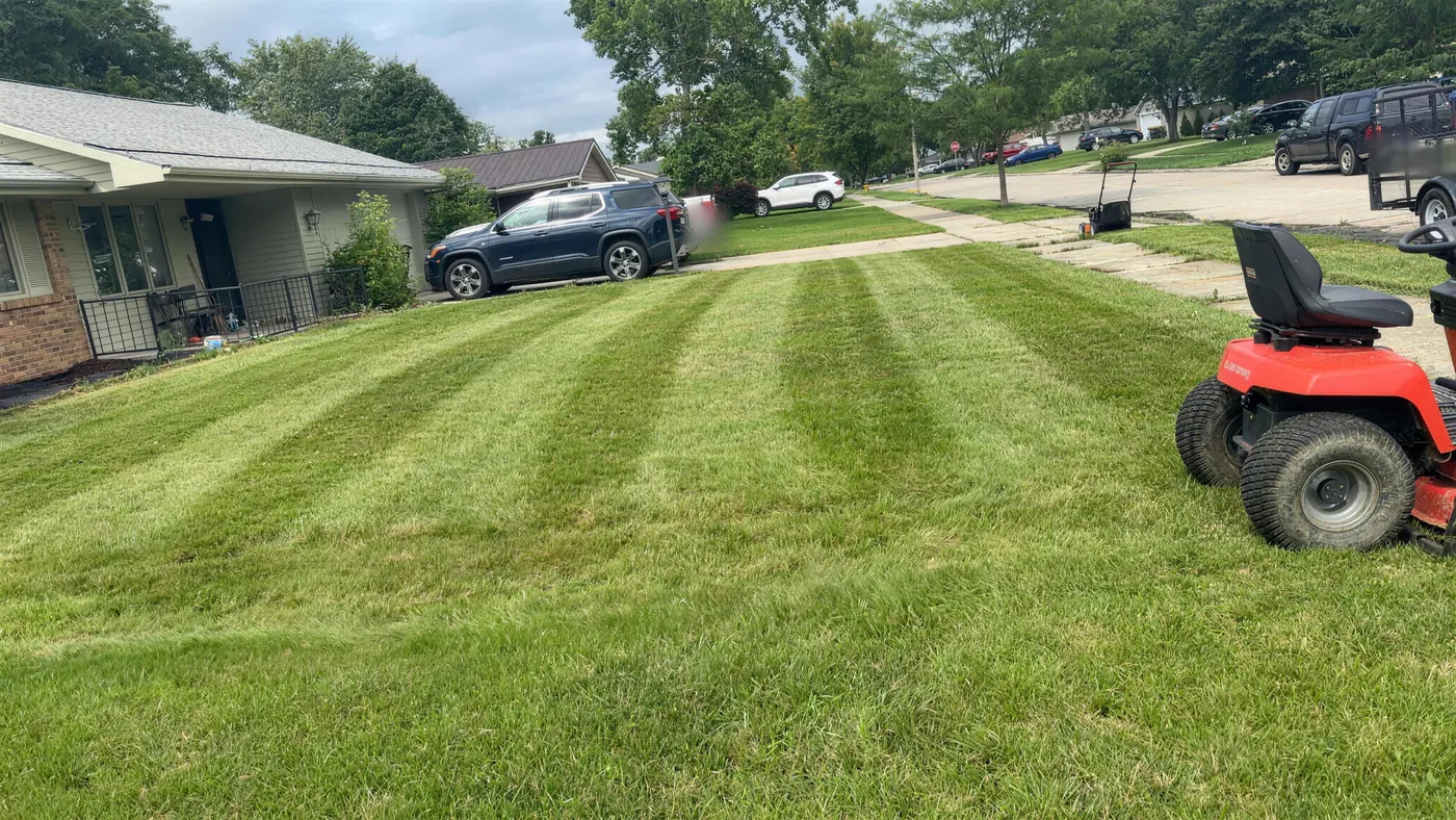 Front lawn mowed in diagonal light and dark stripes, with the riding mower in the corner